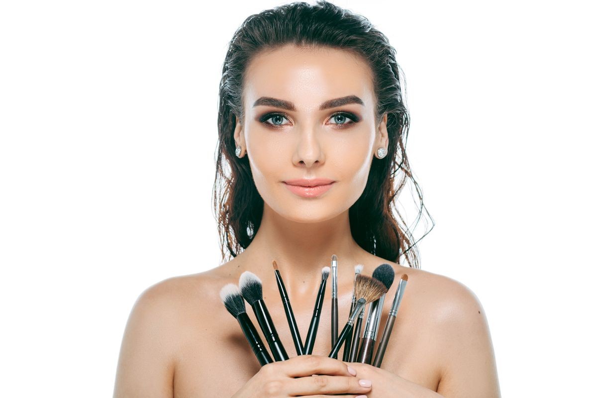 woman face with perfect make-up holding brushes . Portrait of attractive young brunette ,isolated on white , female head looking at camera